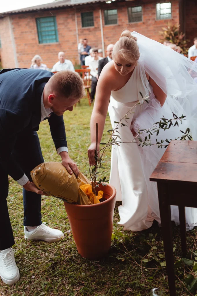Ana e Fred plantam uma muda num vaso durante a cerimônia no jardim