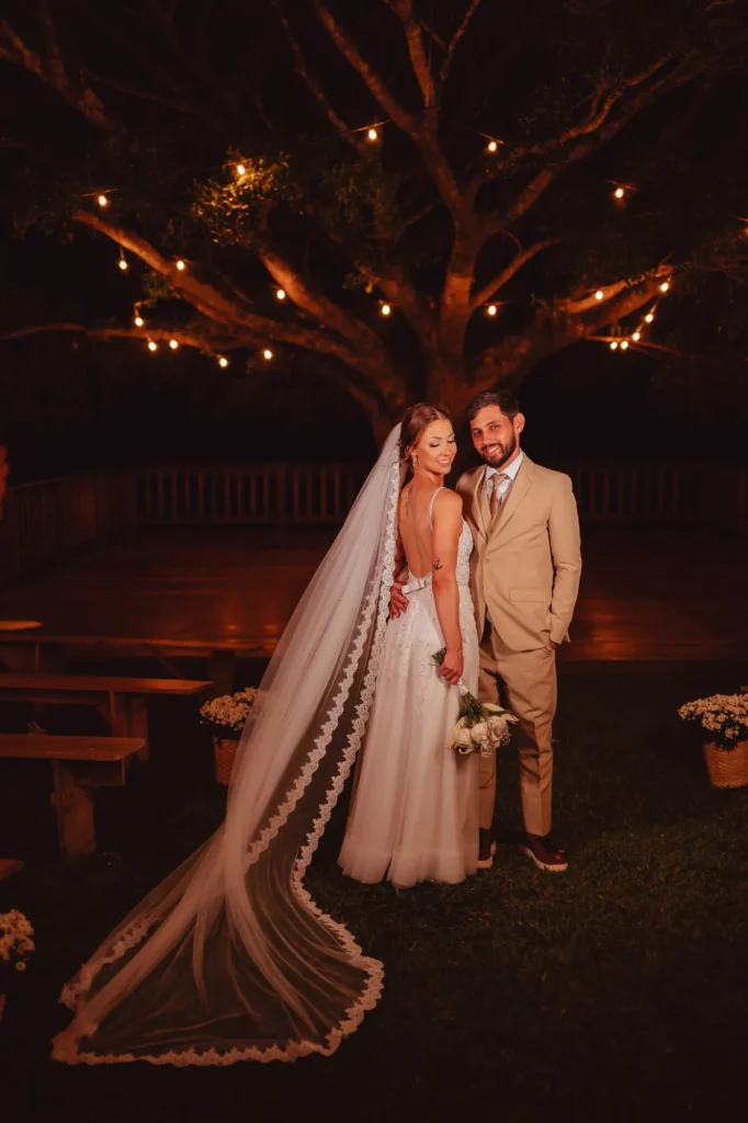 Bruna e Douglas embaixo de uma árvore iluminada, à noite